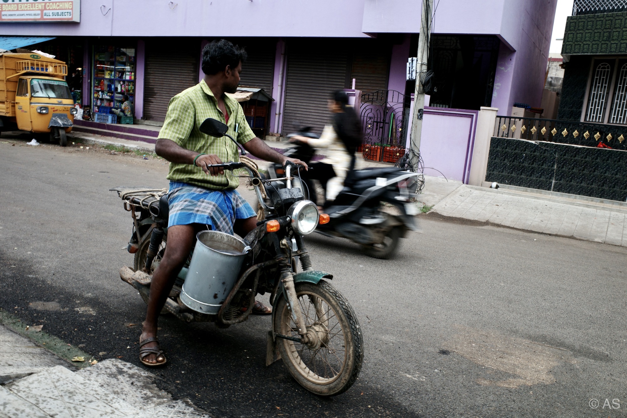 Man on motorcycle carrying milk cans through town